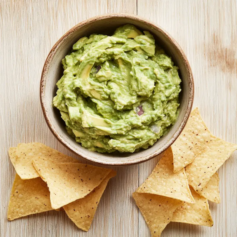 Guacamole maison dans un bol avec tortilla chips sur table bois